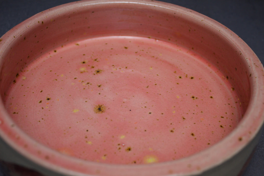 Close-up of a pink ceramic bowl with speckled texture on a dark background