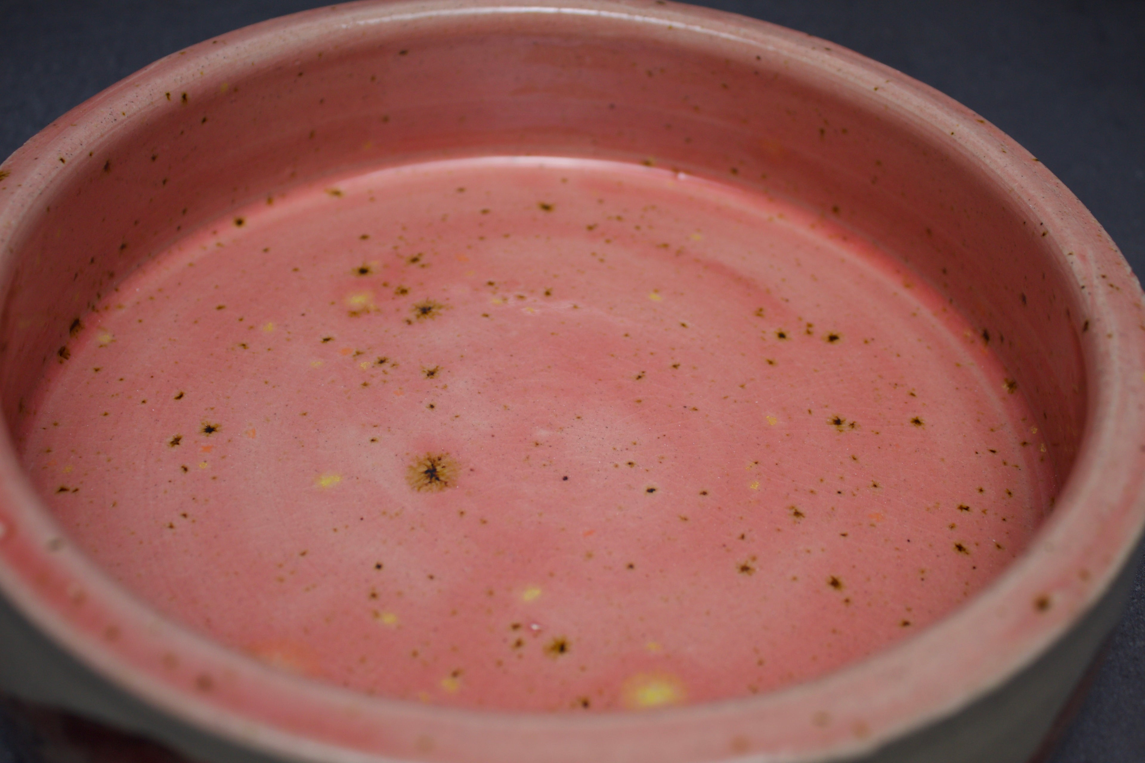 Close-up of a pink ceramic bowl with speckled texture on a dark background